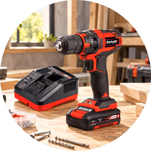 Taladro inalámbrico Einhell rojo y negro con batería y cargador en un banco de trabajo.